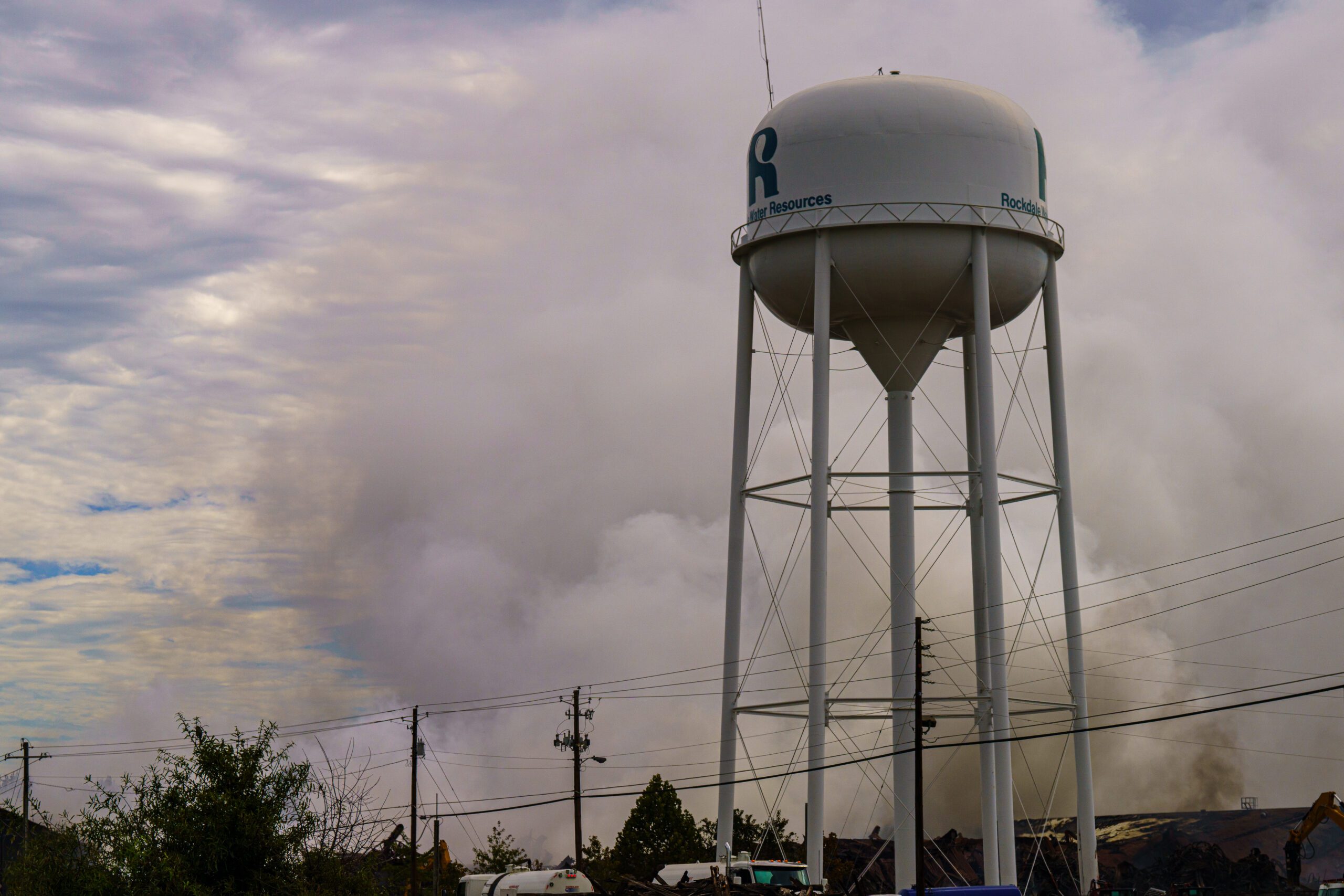 A plume of smoke in the air behind a water tower.