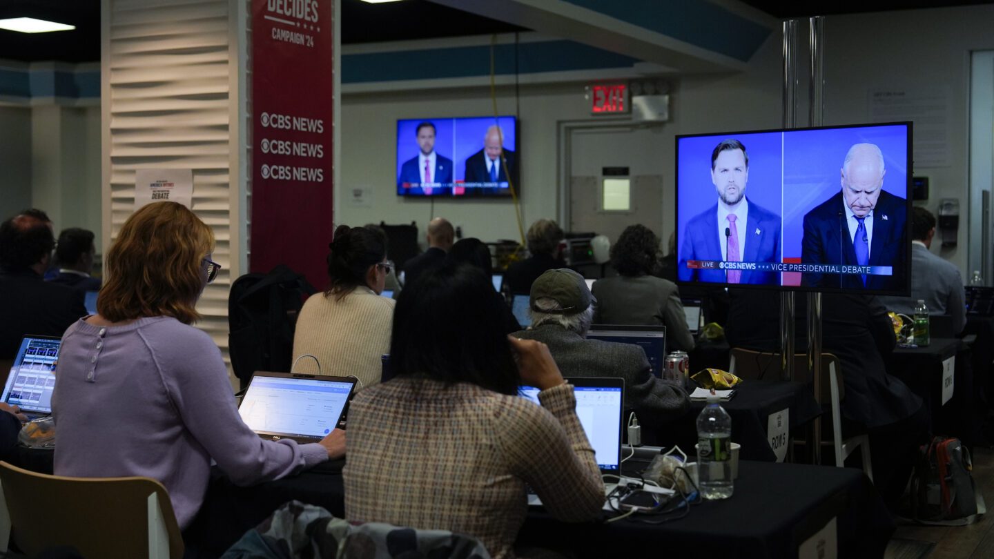 Reporters in the press room watch the vice presidential debate from several TV screens.