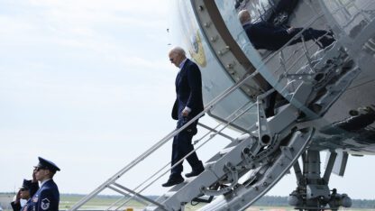 Joe Biden steps down the stairs from Air Force One in an empty lot.