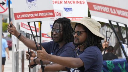 Dockworkers on strike hold up signs.