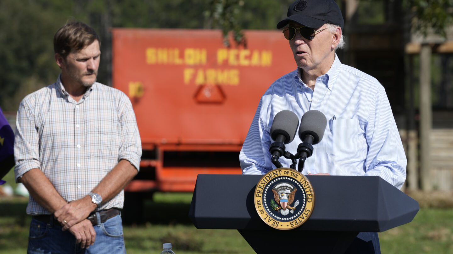 President Joe Biden stands next to Buck Paulk in front of a pecan farm sign, delivering an address.