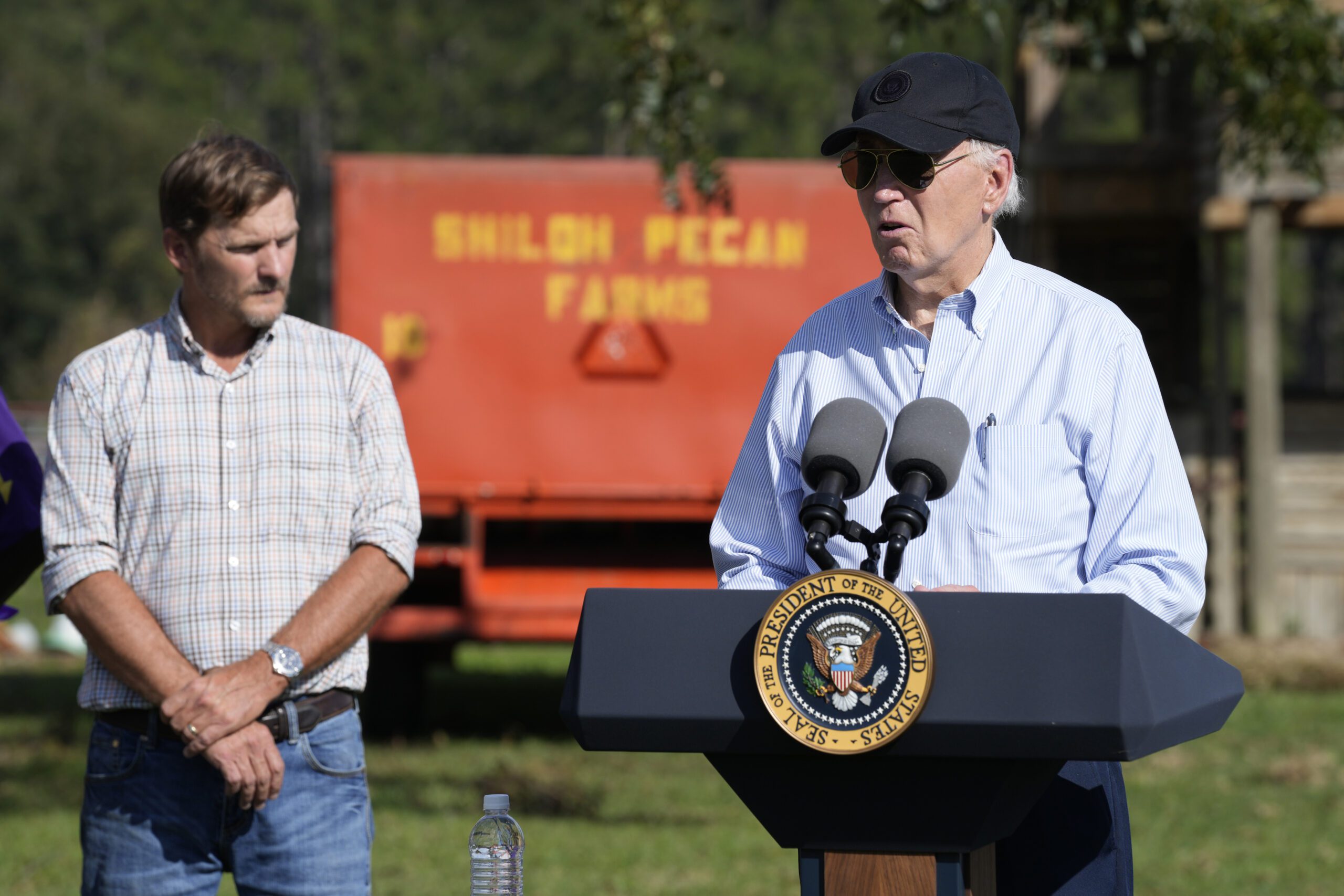 President Joe Biden stands next to Buck Paulk in front of a pecan farm sign, delivering an address.