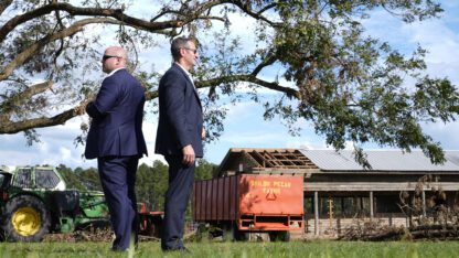 Two members of the Secret Service stand back-to-back at Shiloh Pecan Farm in Georgia as Biden speaks out of the frame.