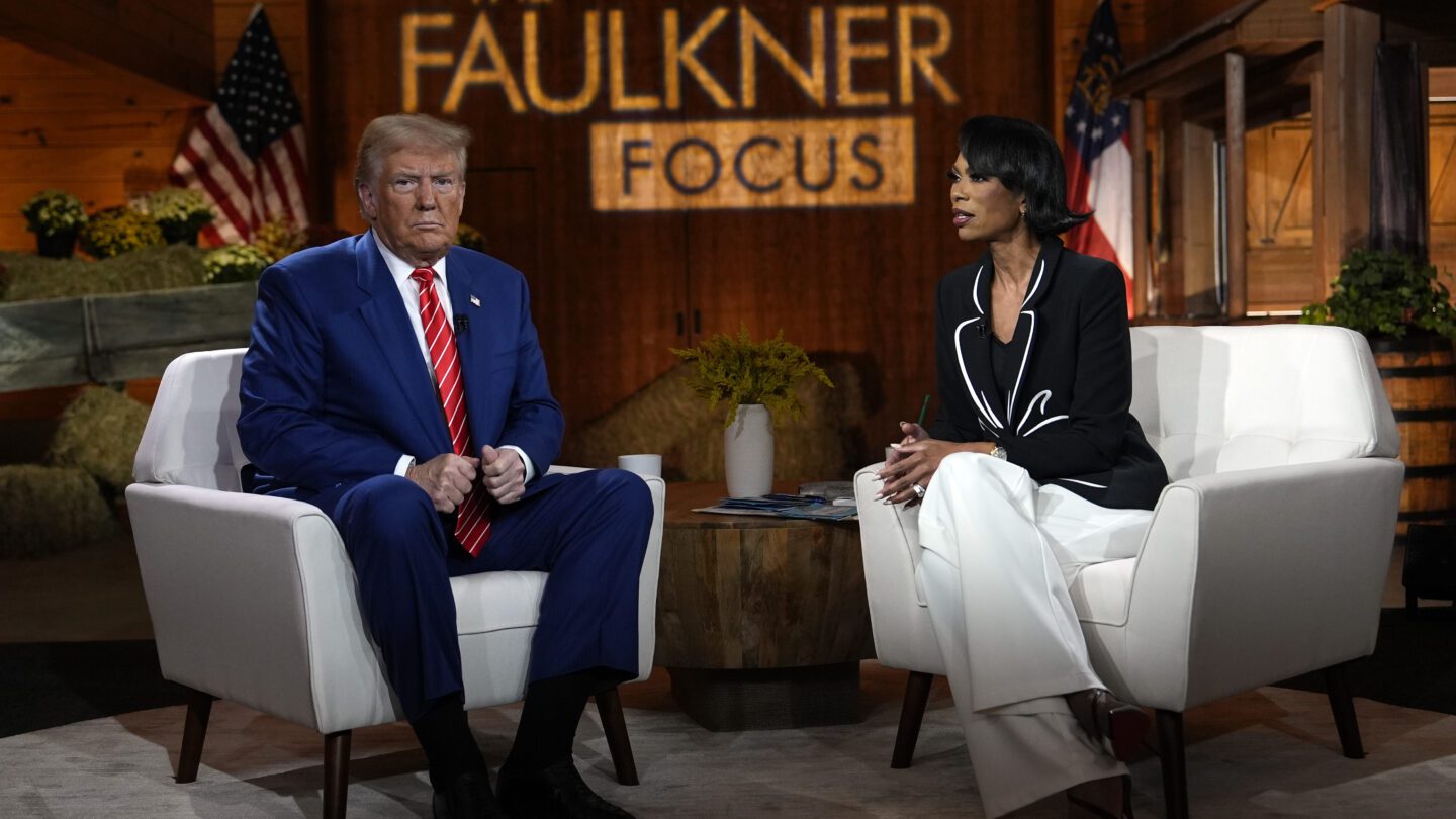 Donald Trump sits on a white armchair to the left, and journalist Harris Faulkner sits in a white armchair to the right. The Faulkner Focus logo is projected onto the wood background.