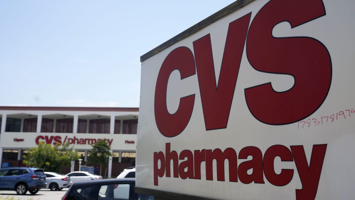 A big CVS sign with red letters and a white background. A CVS store is in the background.