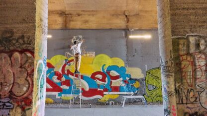 A person stands on a ladder to paint graffiti art.