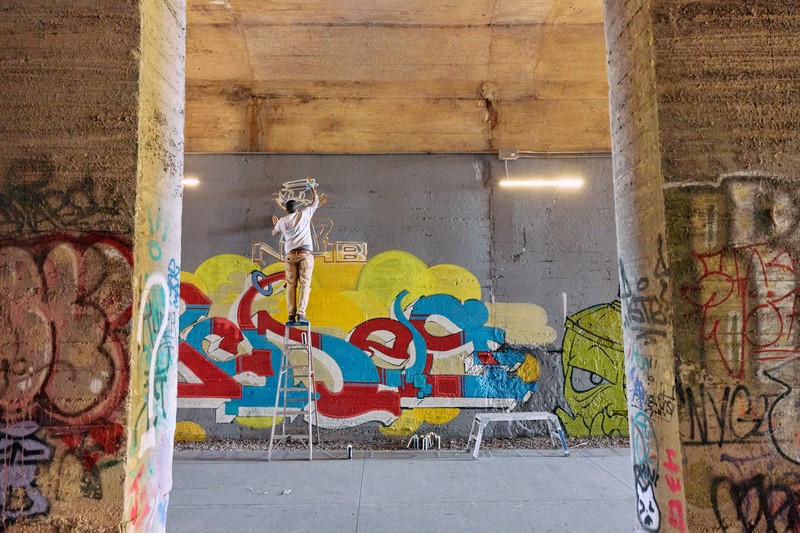 A person stands on a ladder to paint graffiti art.