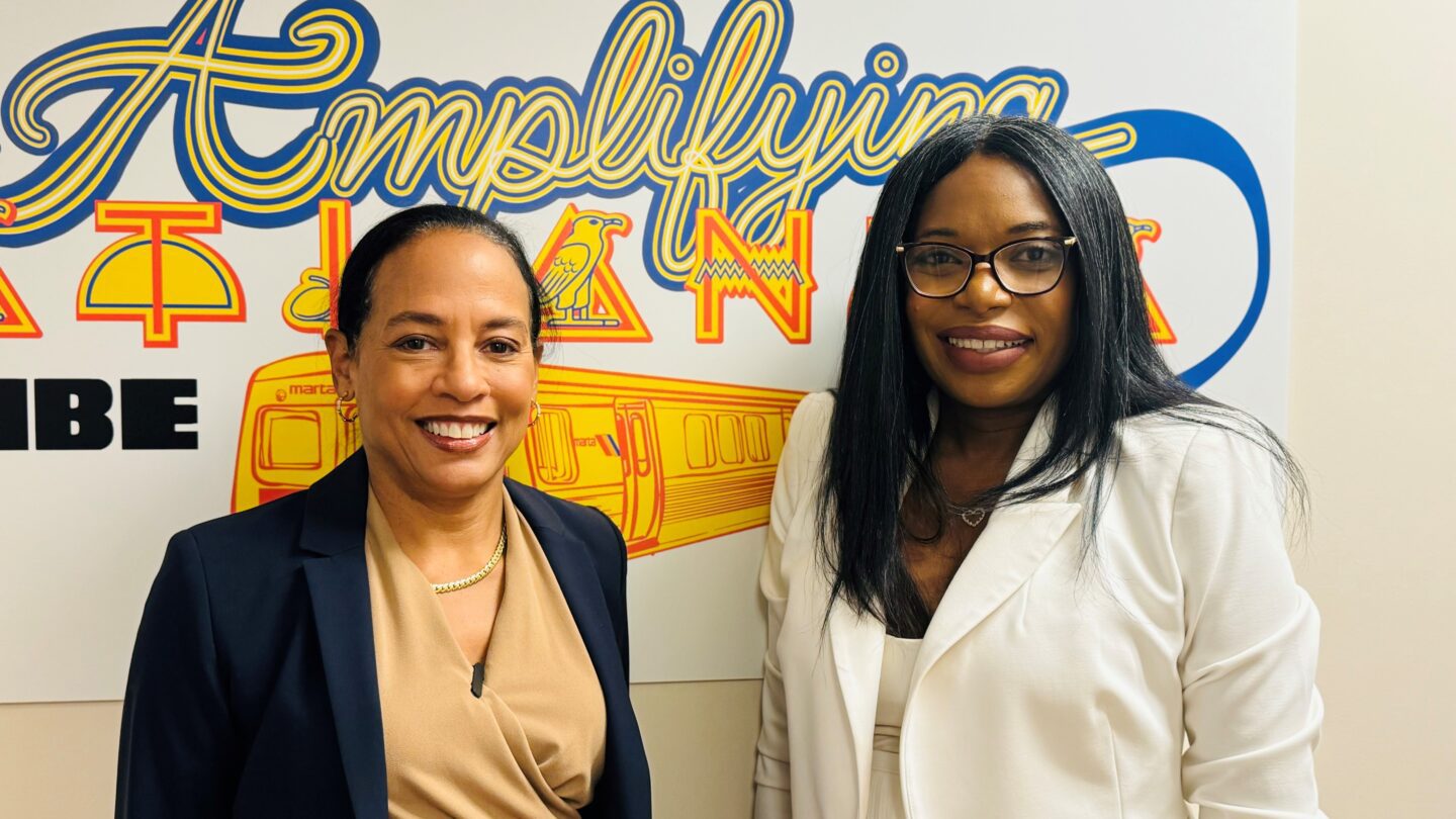 Linder Goler Blount and Tanika Gray Valbrun stand in front of a wall decal that says Amplifying Atlanta.