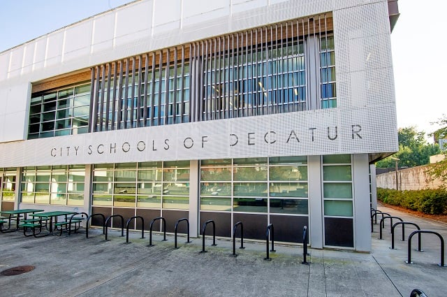 A rectangular building with large windows and a white, modern exterior. There are bars over the windows on the top floor.