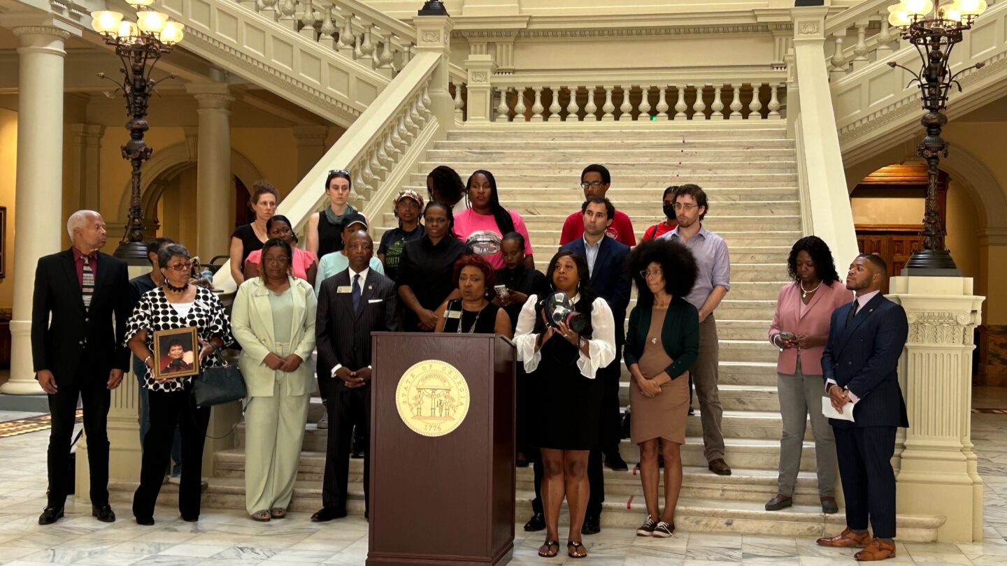 A group of people stand at the bottom of a staircase in the Georgia State Capitol for a press conference.