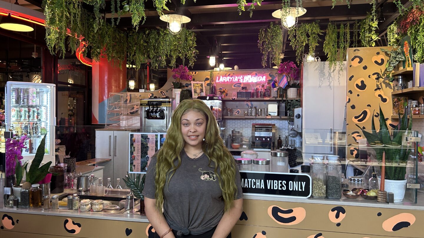 LaRayia Gaston is wearing her green hair and nails stands in front of her cafe.