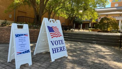 A vote sign in front of a polling location underneath a tree.