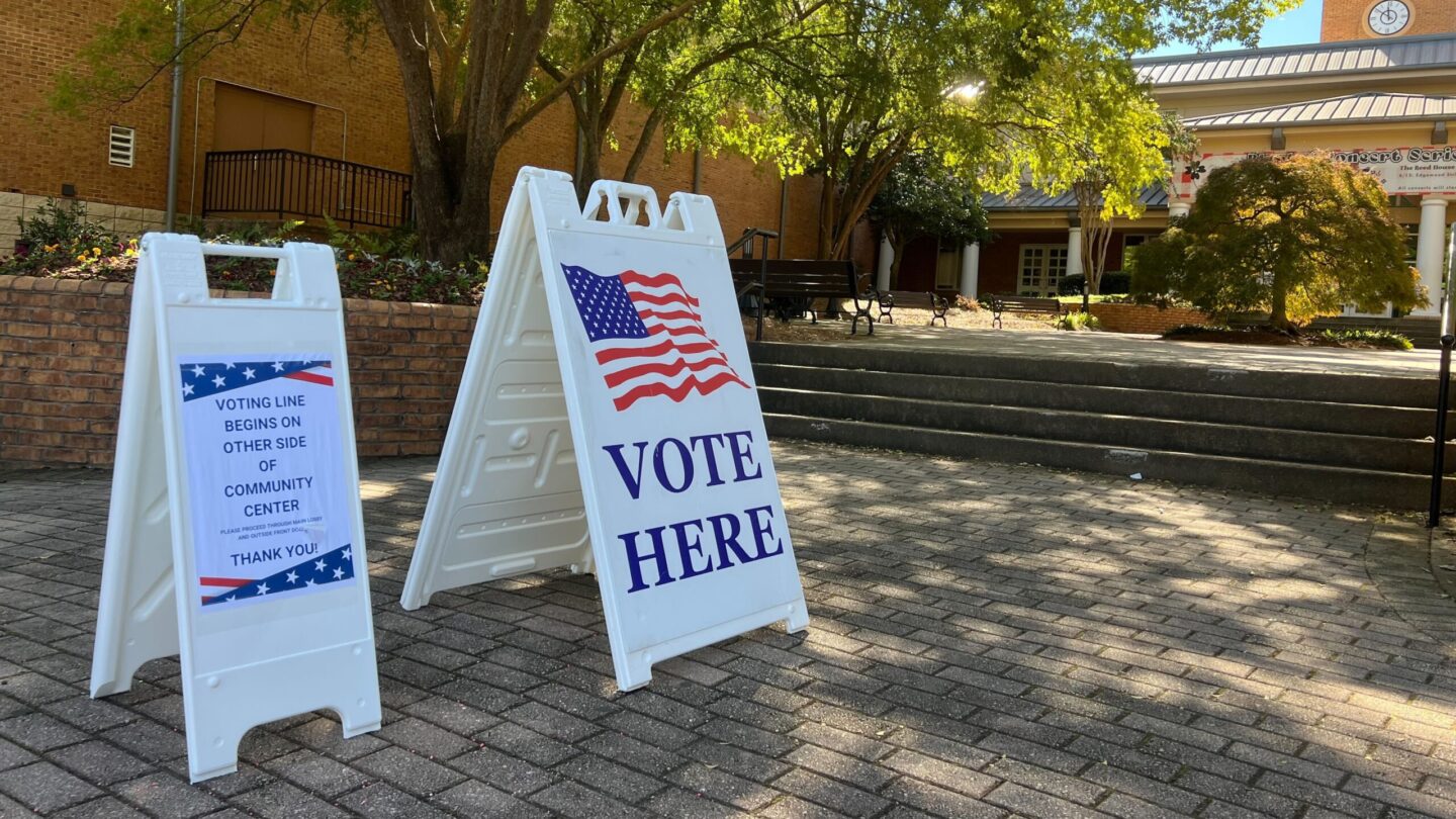 A vote sign in front of a polling location underneath a tree.