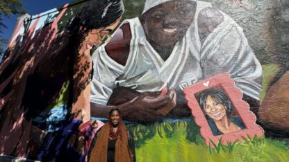 A mural depicting Amber Nicole Thurman and Candi Miller lounging in the grass with smiles on their faces. One woman is holding a pomegranate in her hand.