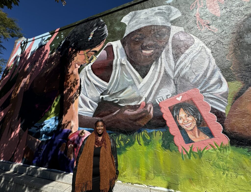 A mural depicting Amber Nicole Thurman and Candi Miller lounging in the grass with smiles on their faces. One woman is holding a pomegranate in her hand.