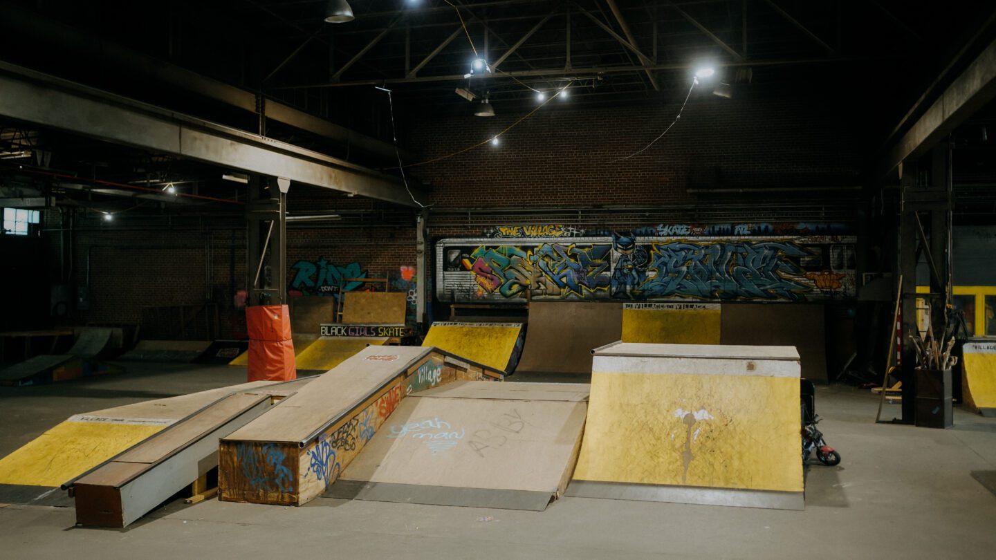 An overhead view of an indoor skatepark, with yellow and wood-colored ramps and graffiti artwork on the walls.