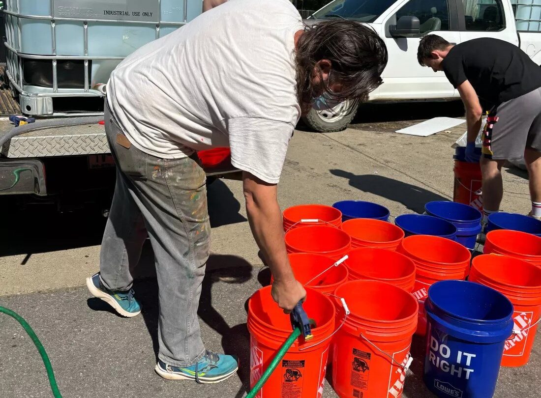 Jerry Cahill fills several orange buckets with a hose.