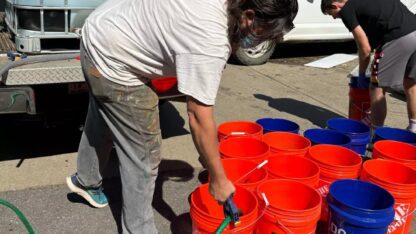 Jerry Cahill fills several orange buckets with a hose.