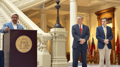 Gabe Sterling speaks at a podium at the Georgia State Capitol. Brad Raffensperger and Blake Evans stand next to him.