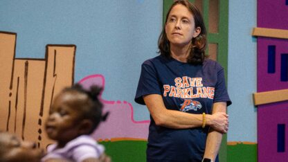 A parent looks off into the distance in front of a colorful wall. A child is in the foreground.