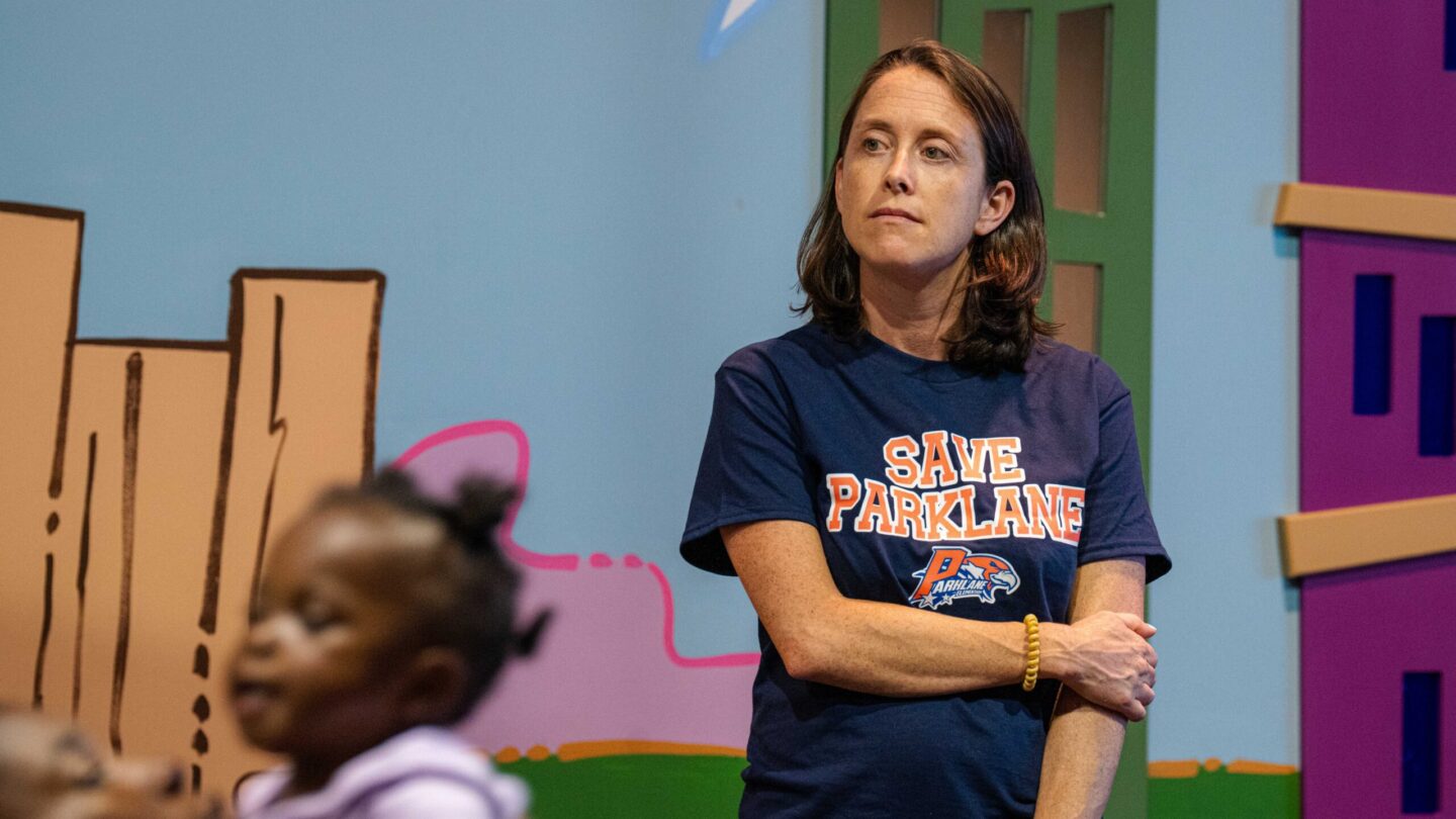 A parent looks off into the distance in front of a colorful wall. A child is in the foreground.