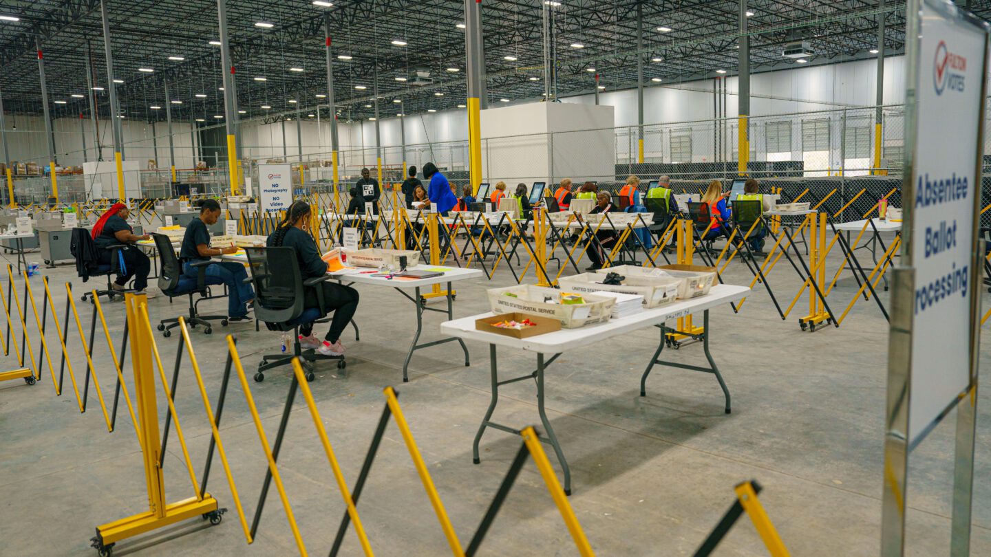 Election workers sit at a row of tables at the Fulton County Elections Hub.