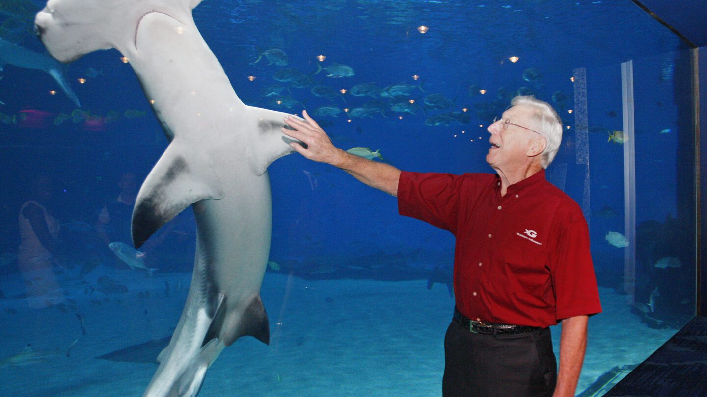 Bernie Marcus stand in front an aquarium tank with a hammerhead shark.