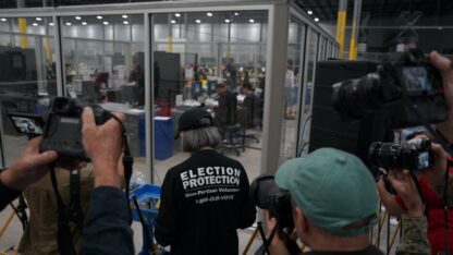 Fulton County election workers upload voting results data from the memory card of the machines used during early voting while observers watch from outside the glass.