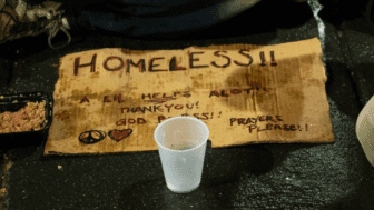 A cardboard sign that says Homeless next to a plastic cup.