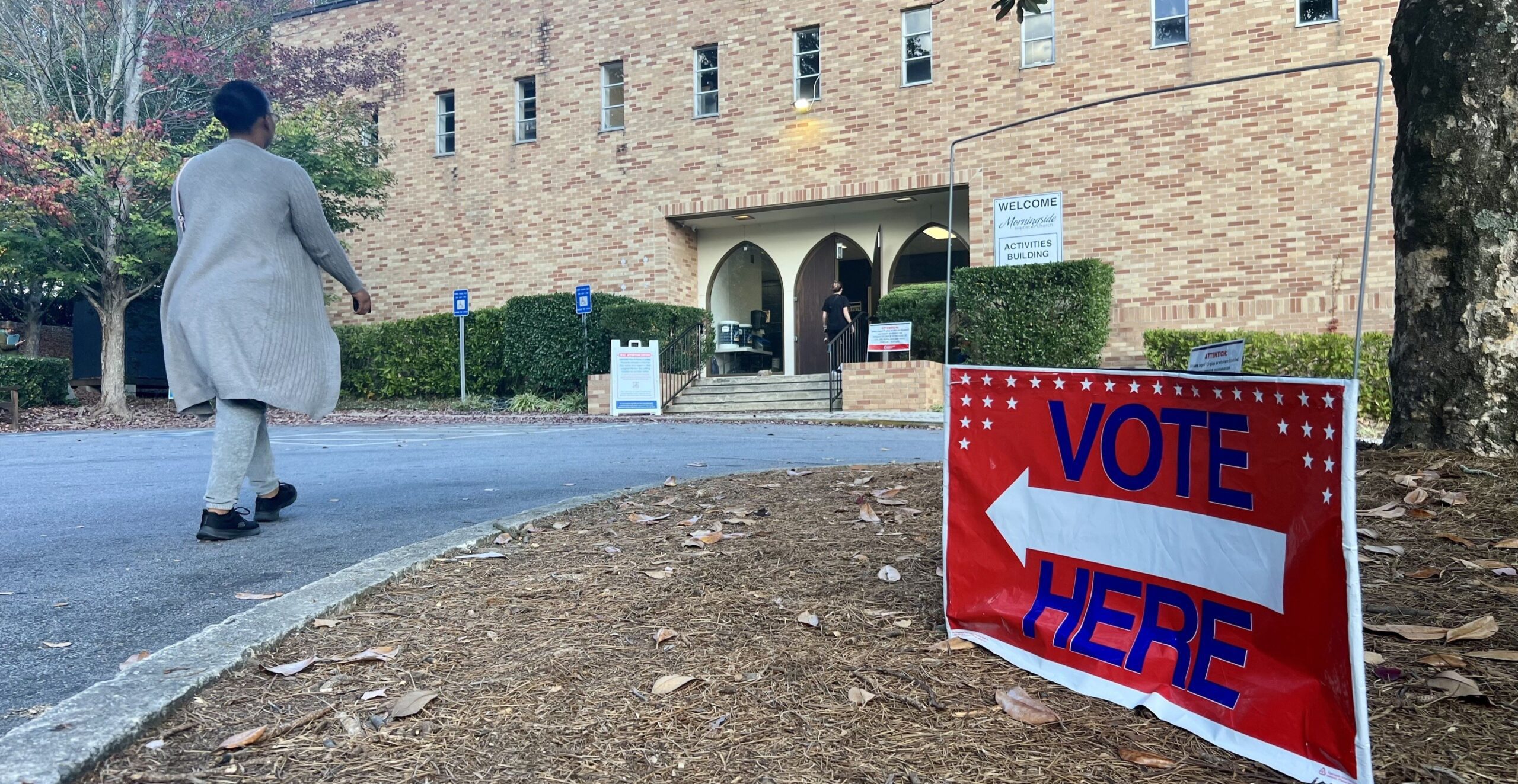 A person walks toward Morningside Church in Midtown Atlanta next to a red Vote Here sign.