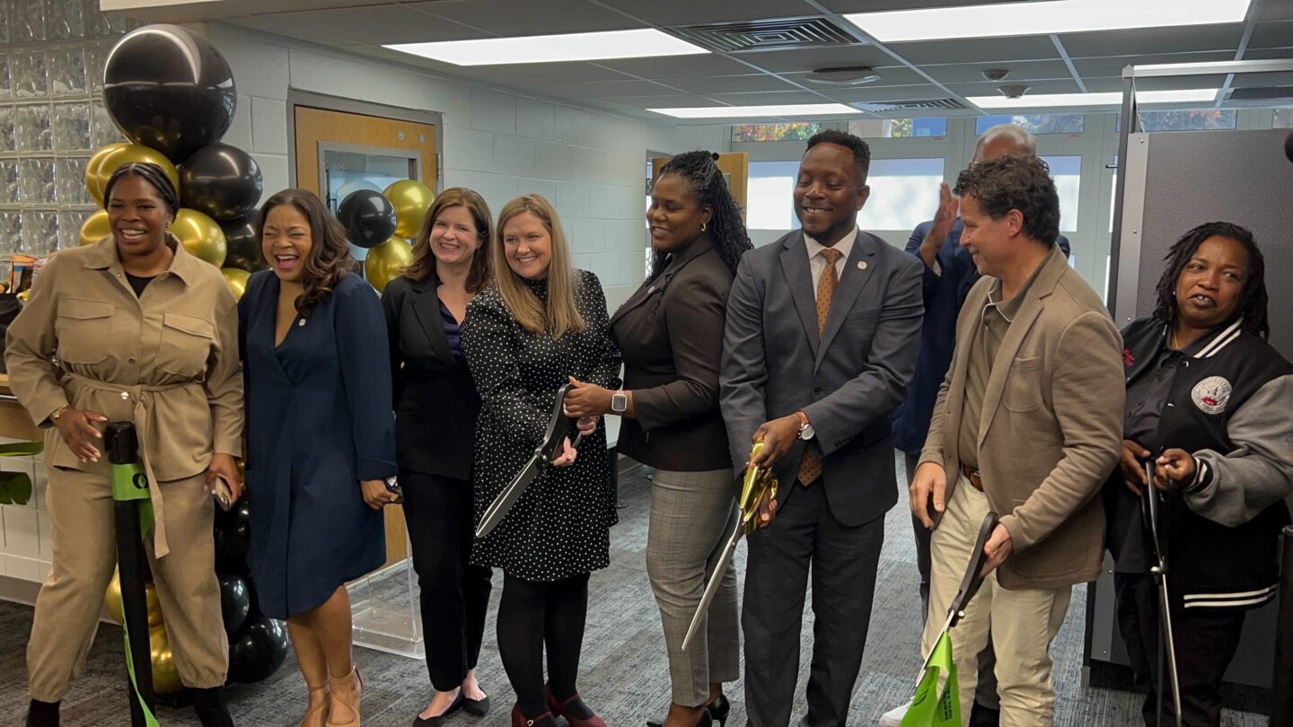 A group of people hold scissors at a ribbon-cutting event.