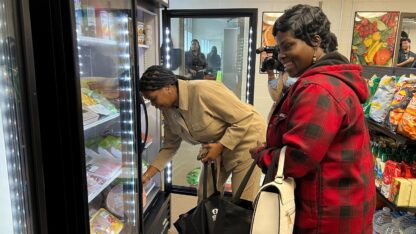 Jasmine Crowe-Houston bends down to pick up an item from a freezer. Leandre Bigby stands next to her.