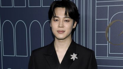 BTS member Jimin wearing a black suit and a broach.