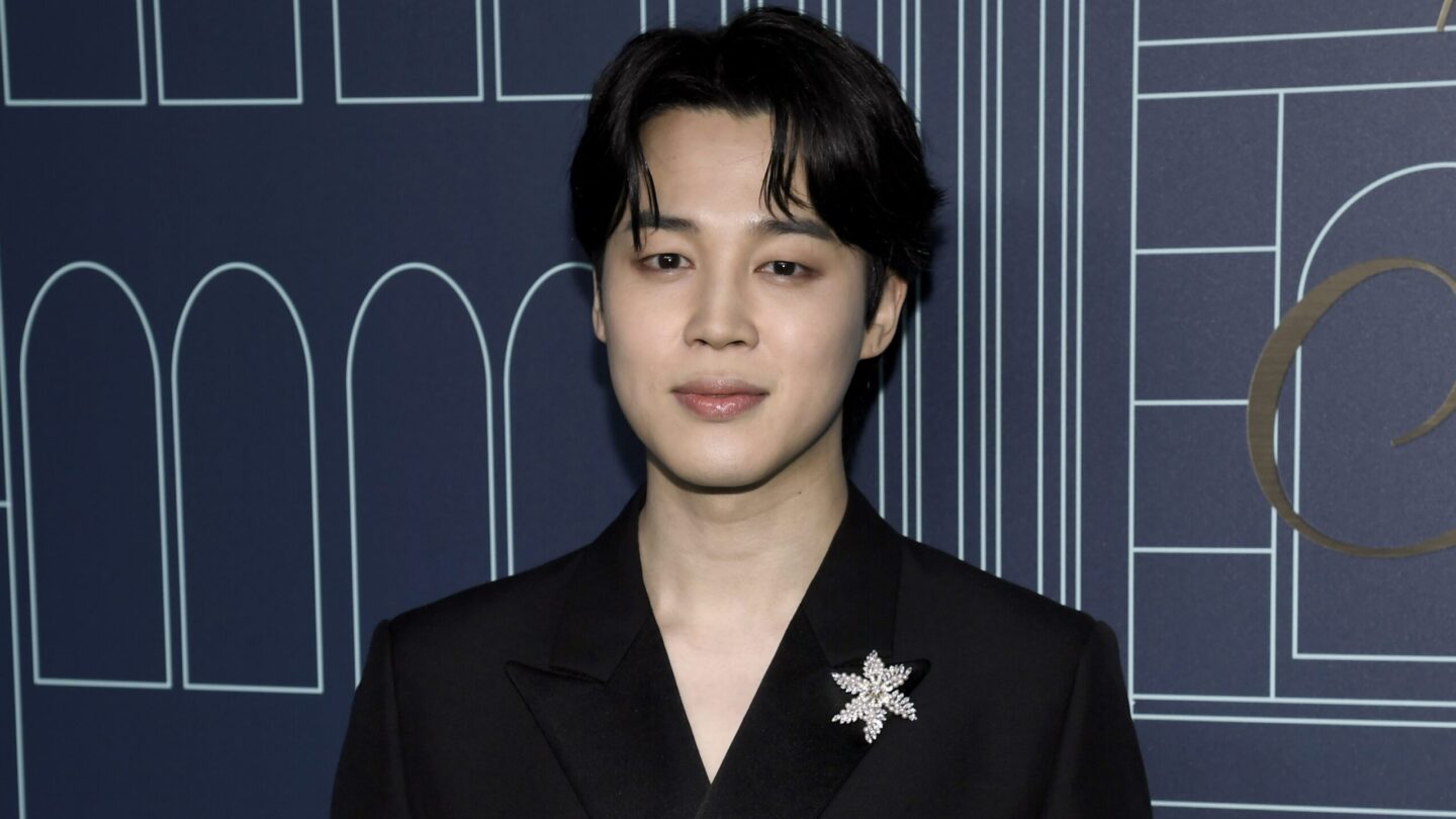 BTS member Jimin wearing a black suit and a broach.