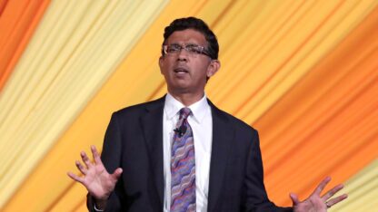 Dinesh D'Souza speaks in front of an orange background.