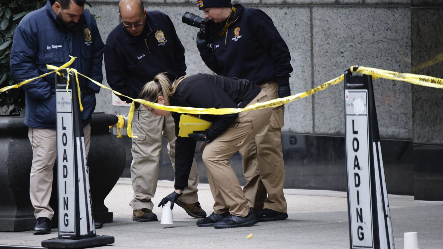 Multiple law enforcement menbers kneeling near the scene of a crime in Manhattan.