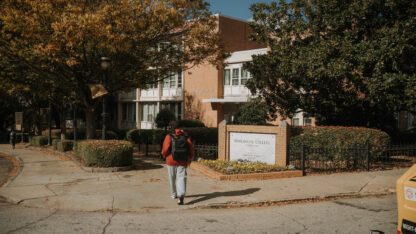 A student walks toward a building on the Morehouse College campus, next to a sign with the college's name on it.