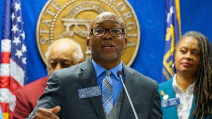 Georgia Senate Minority Leader Harold Jones at a presser in front of a blue background, a gold seal and several flags. He stands next to other Democrats.