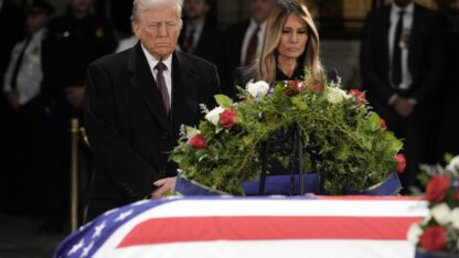 Donald and Melania Trump stand in front of the flag-draped casket of former President Jimmy Carter.